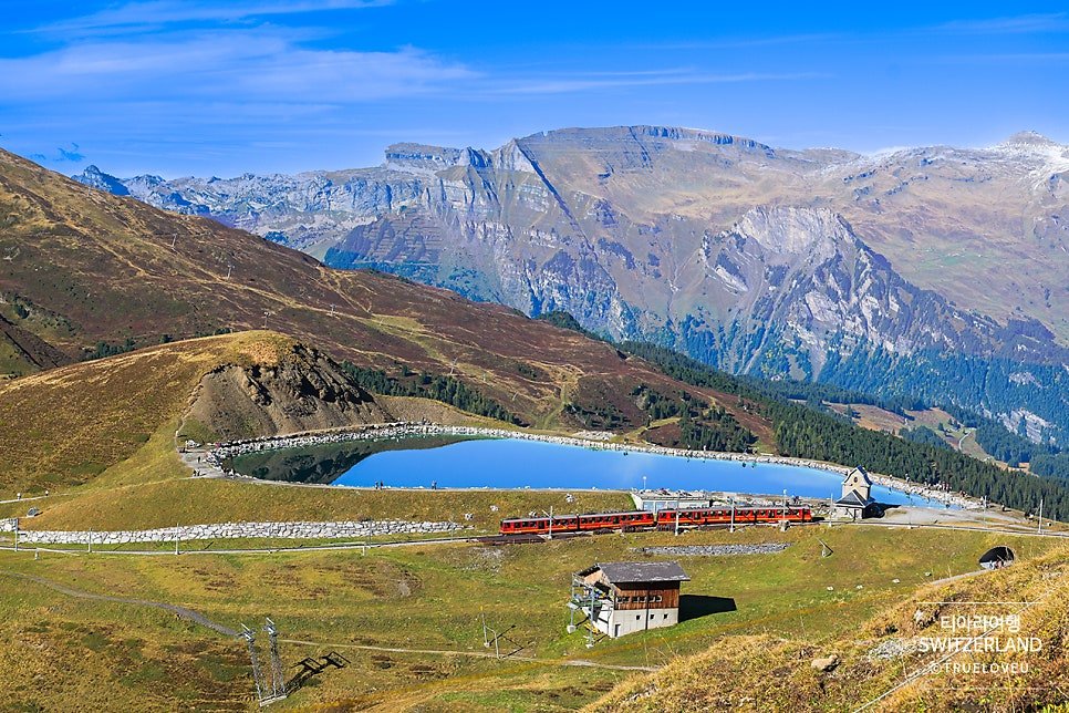 Scenic mountain lake and red cogwheel train along the Jungfraujoch VIP hiking trail in Switzerland