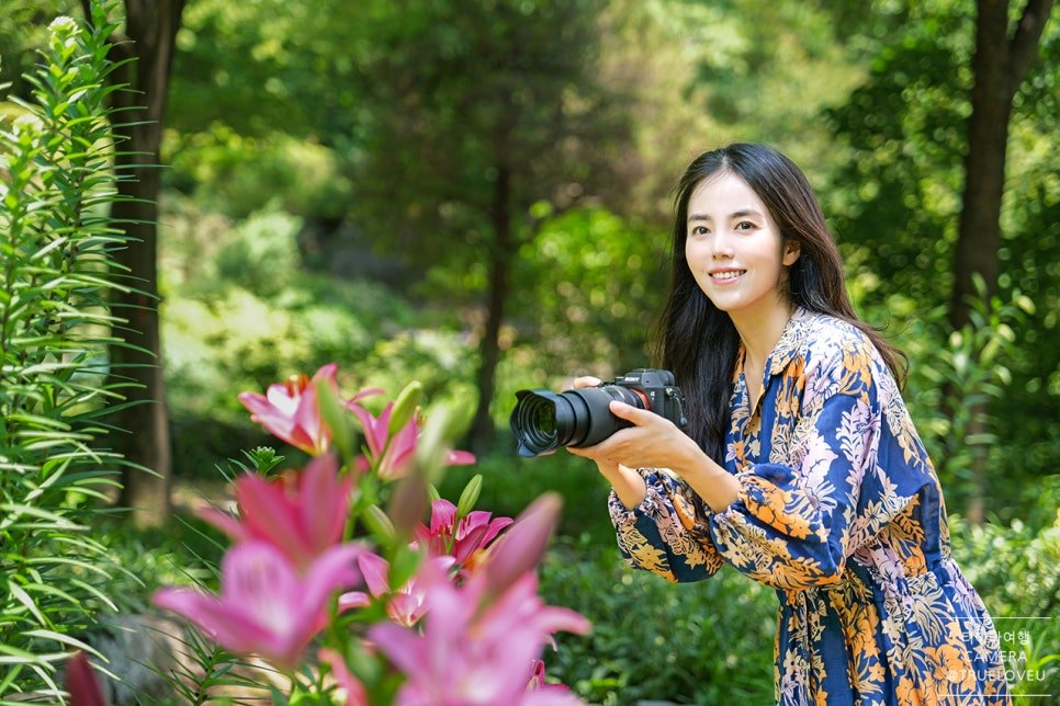 Woman photographing pink lilies with a TAMRON lens on a mirrorless camera
