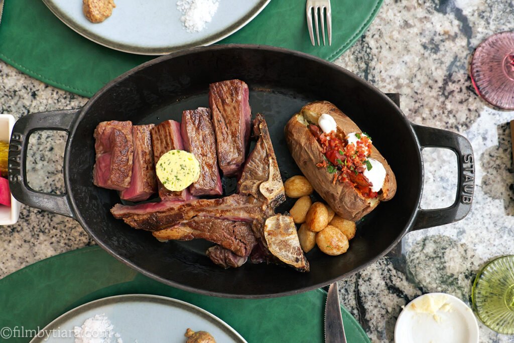 US Prime dry aged ribeye steak with Roasted garlic, baked potato, and pickles served with the ribeye