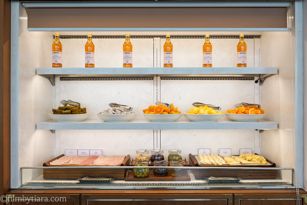 Dessert and cheese bar display with ade bottles, pickles, citrus, and cold cuts at Restaurant Voisin