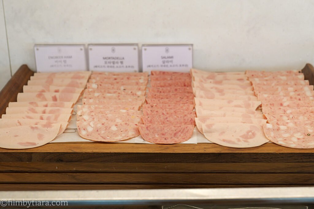 Sliced ham, mortadella, and salami on a wooden tray at the Voisin cheese bar